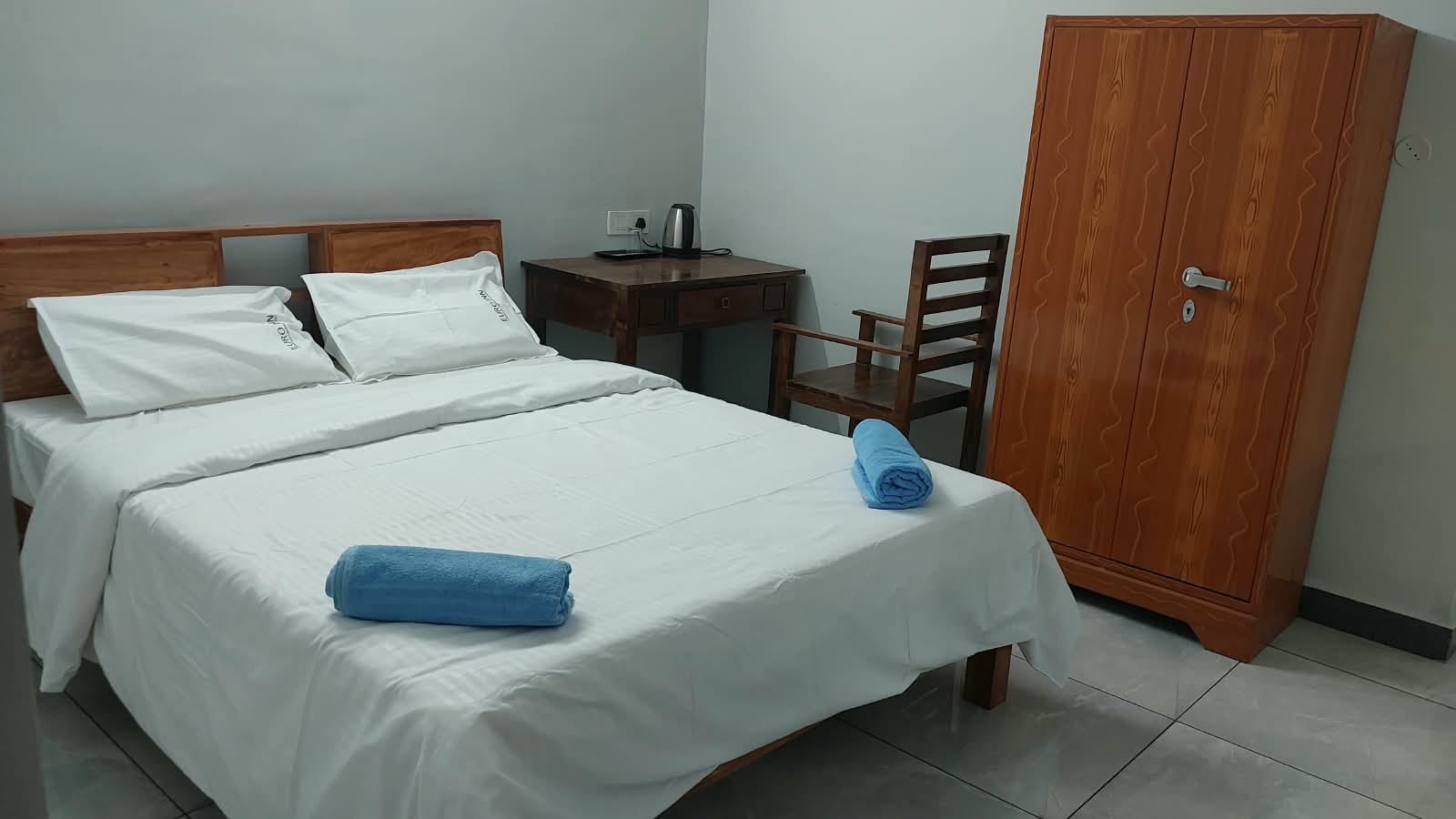 Bedroom with a double bed, desk, kettle and wooden wardrobe.