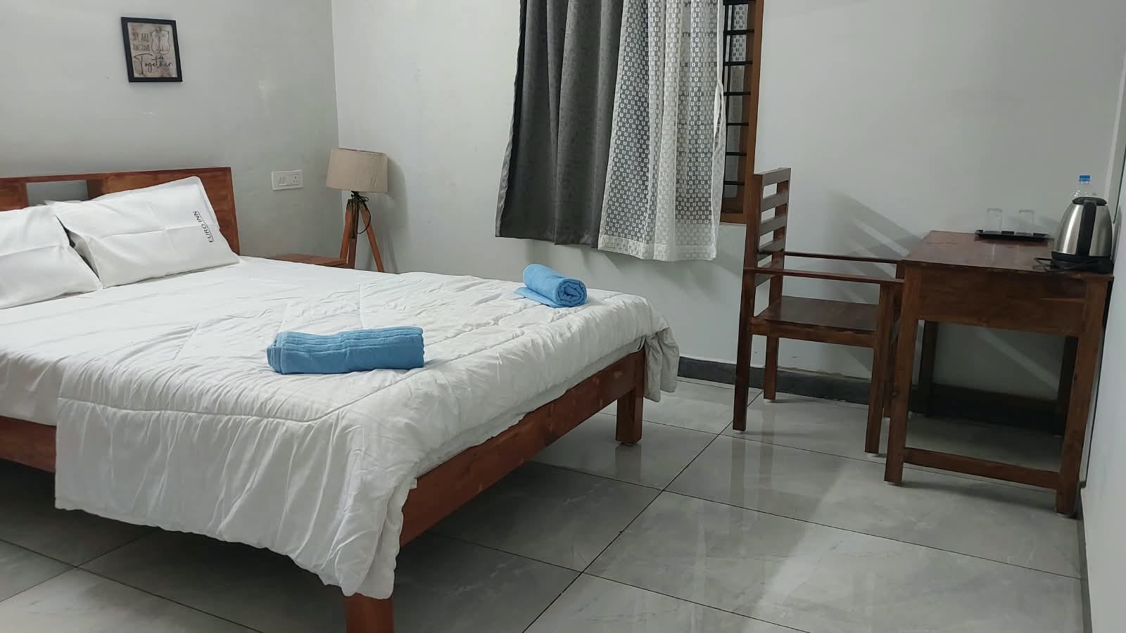 Bedroom with folded blue towels on the bed and a desk beside the window.