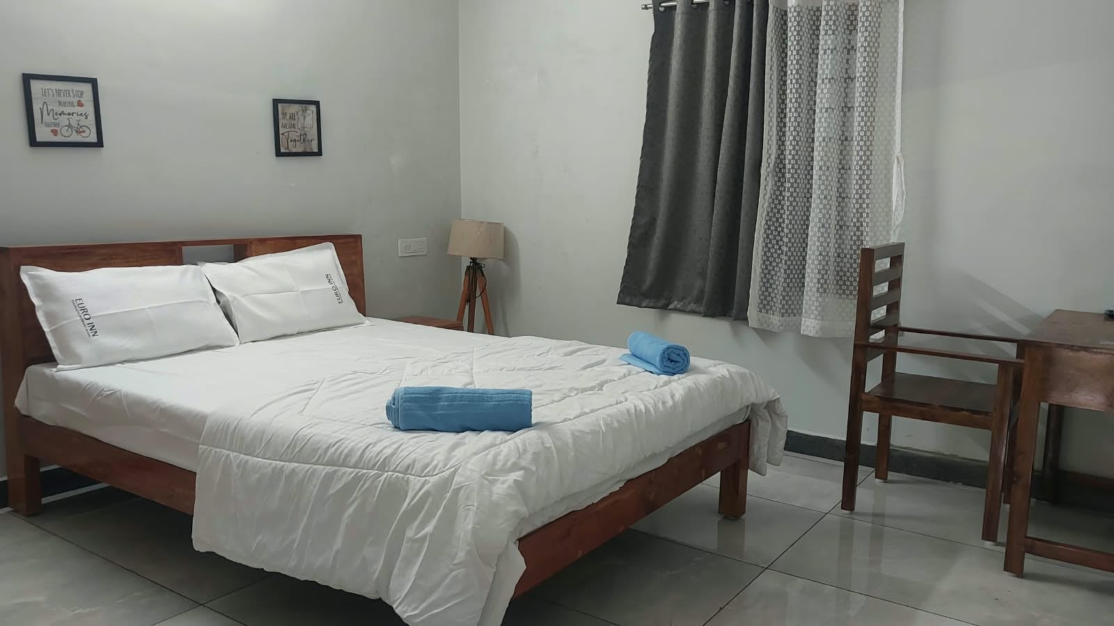Bedroom with a double bed, blue towels, curtains and a writing desk.